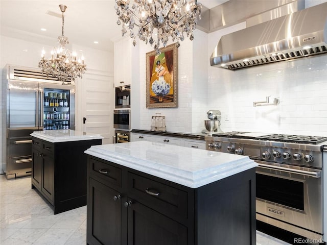 kitchen with high end appliances, a notable chandelier, light stone counters, a kitchen island, and wall chimney exhaust hood