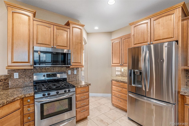 kitchen with light tile patterned flooring, stainless steel appliances, and dark stone counters