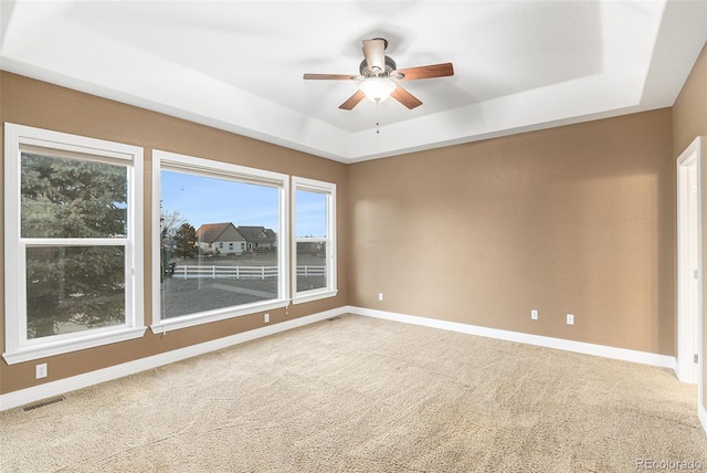 carpeted spare room featuring ceiling fan and a raised ceiling