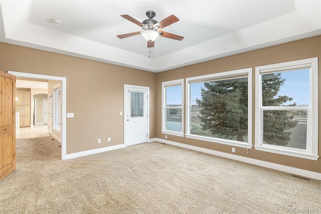 empty room with a tray ceiling, ceiling fan, and light carpet