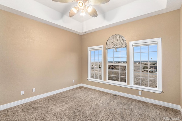 carpeted spare room with a tray ceiling, plenty of natural light, and ceiling fan