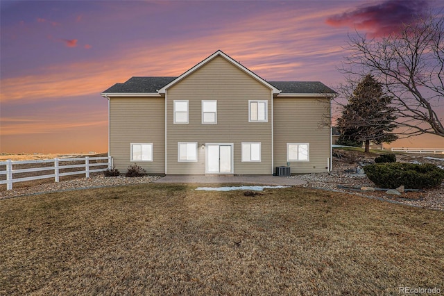 back house at dusk with a yard, a patio area, and central air condition unit