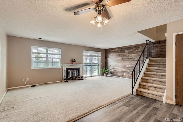unfurnished living room with a textured ceiling, stairs, plenty of natural light, and wood walls