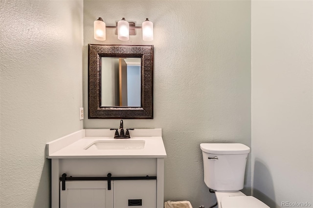 half bathroom with vanity, toilet, and a textured wall