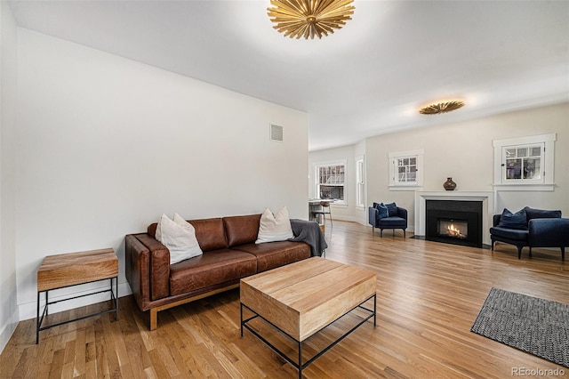 living room featuring a warm lit fireplace, baseboards, visible vents, and light wood-style floors