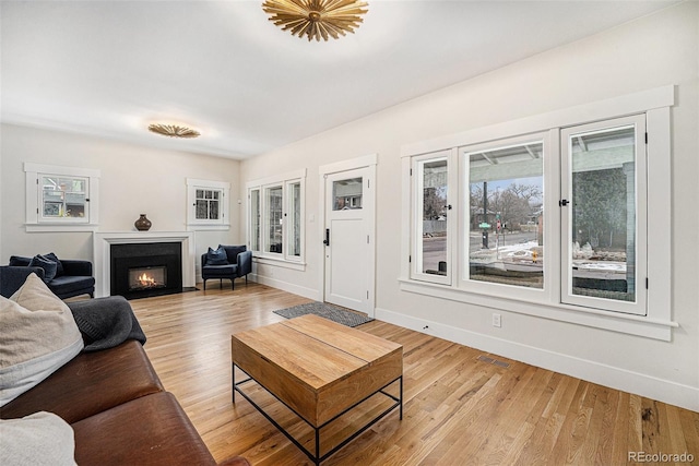 living room featuring a warm lit fireplace, light wood-style floors, and a wealth of natural light