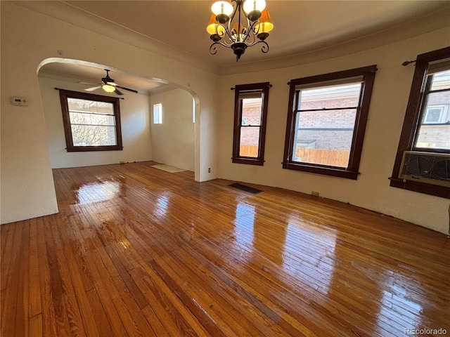 empty room featuring visible vents, hardwood / wood-style floors, ceiling fan with notable chandelier, and arched walkways