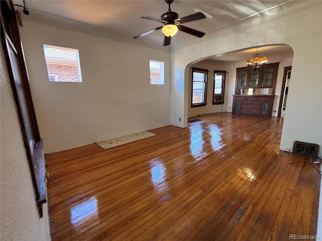 empty room featuring arched walkways, wood-type flooring, and ceiling fan with notable chandelier