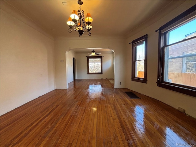 unfurnished dining area with a chandelier, wood-type flooring, visible vents, and arched walkways