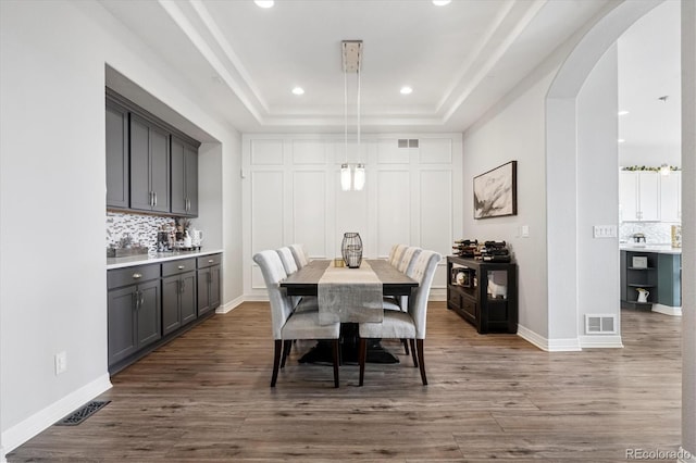 dining space with arched walkways, wood finished floors, visible vents, and a raised ceiling