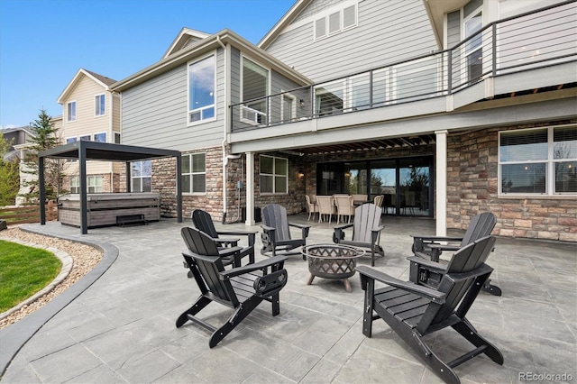rear view of property featuring stone siding, a hot tub, a balcony, a patio, and an outdoor fire pit