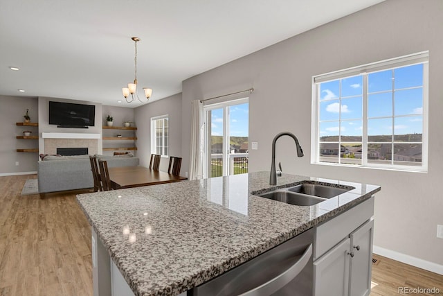 5166 Trails Edge Ln, Castle Rock, CO 80104 - kitchen with a sink, stainless steel dishwasher, an island with sink, light wood-type flooring, and a fireplace