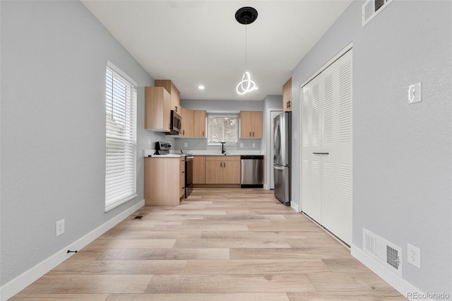 kitchen with light brown cabinetry, light wood-type flooring, stainless steel appliances, sink, and decorative light fixtures