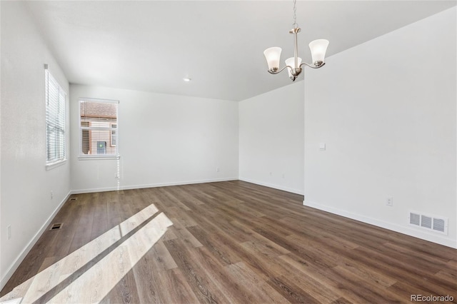 spare room featuring a chandelier and dark wood-type flooring