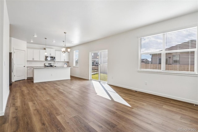 kitchen featuring stainless steel appliances, decorative light fixtures, white cabinets, hardwood / wood-style floors, and a center island