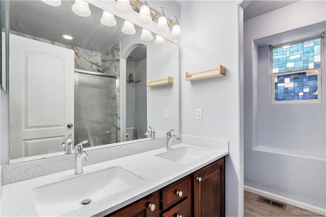 bathroom with a stall shower, toilet, wood finished floors, double vanity, and baseboards