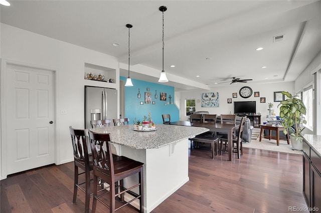 kitchen with dark hardwood / wood-style flooring, ceiling fan, stainless steel refrigerator with ice dispenser, pendant lighting, and a kitchen bar