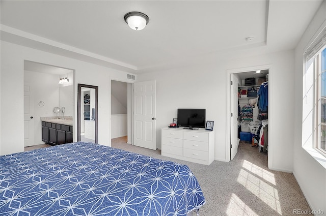 bedroom featuring a closet, a walk in closet, connected bathroom, and light carpet