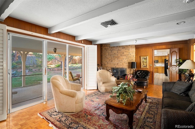 living area featuring beamed ceiling, wooden walls, a fireplace, a textured ceiling, and visible vents