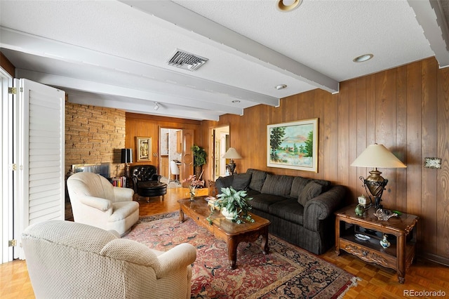 living area with a textured ceiling, beamed ceiling, visible vents, and wood walls