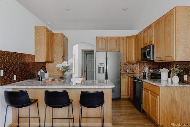 1131 N 4th St, Johnstown, CO 80534 - kitchen featuring stainless steel appliances, a peninsula, a breakfast bar area, light wood-style flooring, and decorative backsplash