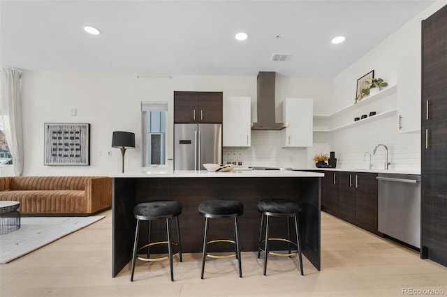 kitchen featuring visible vents, wall chimney range hood, a breakfast bar, light countertops, and appliances with stainless steel finishes