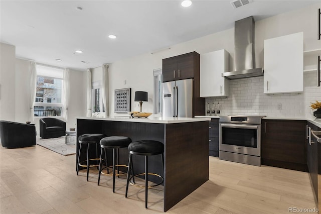 kitchen featuring appliances with stainless steel finishes, wall chimney exhaust hood, light countertops, and a breakfast bar