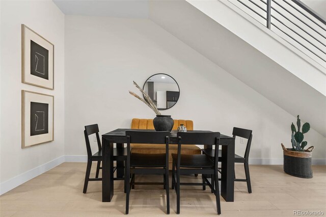 dining area with light wood-type flooring, baseboards, and vaulted ceiling