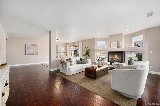 living room featuring visible vents, dark wood-type flooring, baseboards, and a glass covered fireplace