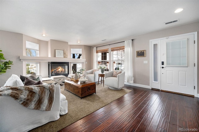 living room featuring baseboards, visible vents, dark wood finished floors, a textured ceiling, and a glass covered fireplace