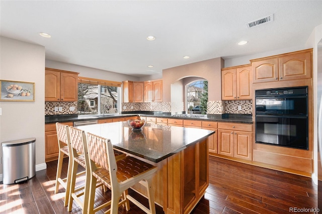 kitchen with visible vents, a center island, dark wood-type flooring, a kitchen bar, and dobule oven black