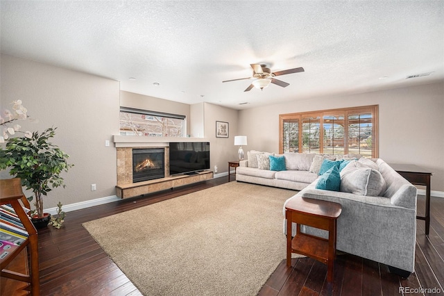 living room featuring dark wood-style floors, visible vents, a tile fireplace, and baseboards