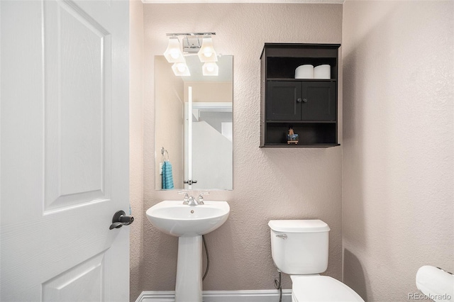 half bath featuring a sink, toilet, and a textured wall