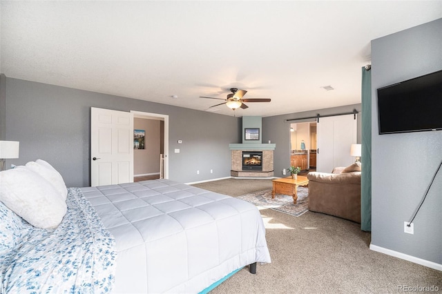 bedroom featuring ceiling fan, baseboards, a barn door, carpet flooring, and a glass covered fireplace