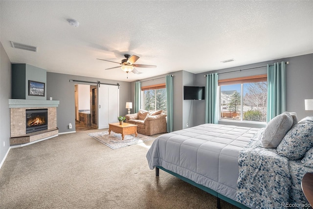 carpeted bedroom with a tiled fireplace, a barn door, visible vents, and a textured ceiling