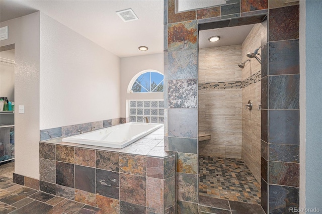 bathroom with a garden tub, stone tile floors, visible vents, and a tile shower