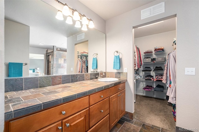 bathroom featuring stone tile floors, visible vents, a spacious closet, and vanity