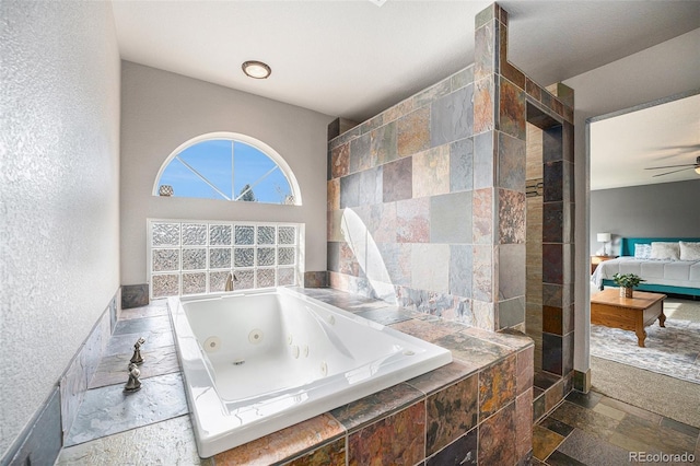 bathroom with connected bathroom, stone tile floors, a ceiling fan, and a tub with jets