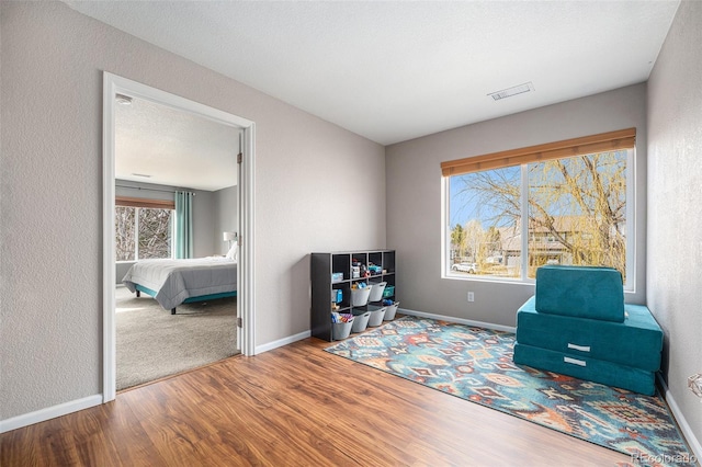 living area with wood finished floors, visible vents, a textured wall, and baseboards