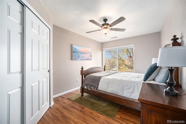 bedroom featuring visible vents, dark wood-type flooring, baseboards, a closet, and a textured ceiling