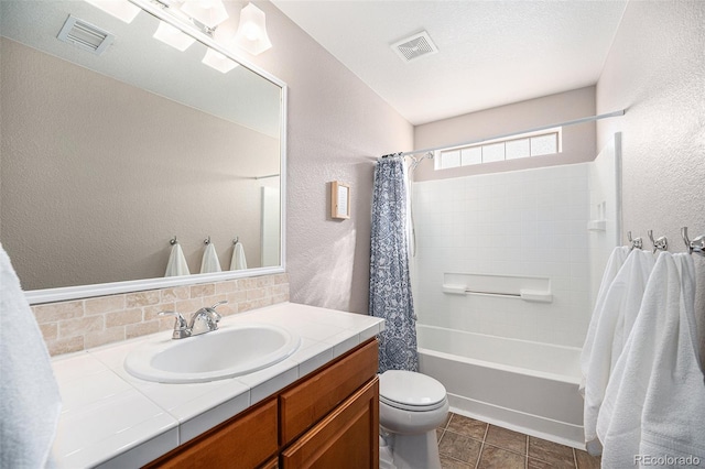 full bath featuring vanity, toilet, a textured wall, and visible vents