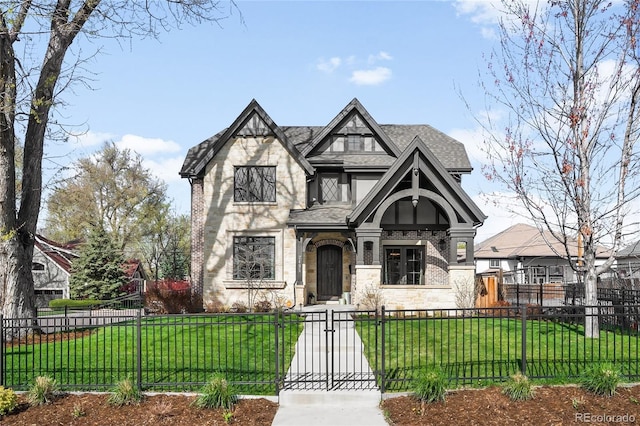 tudor house with a fenced front yard, roof with shingles, a front lawn, and stone siding