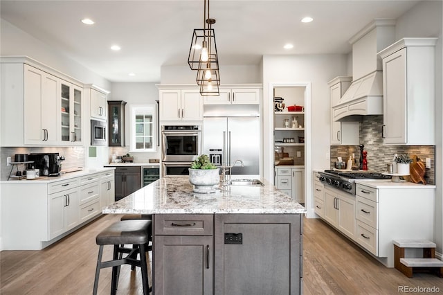 kitchen with built in appliances, an island with sink, a sink, and tasteful backsplash