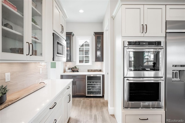 kitchen with wine cooler, built in appliances, tasteful backsplash, and light wood-type flooring