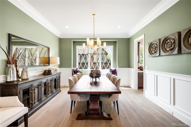 dining space with wainscoting, a notable chandelier, ornamental molding, a decorative wall, and light wood-style flooring
