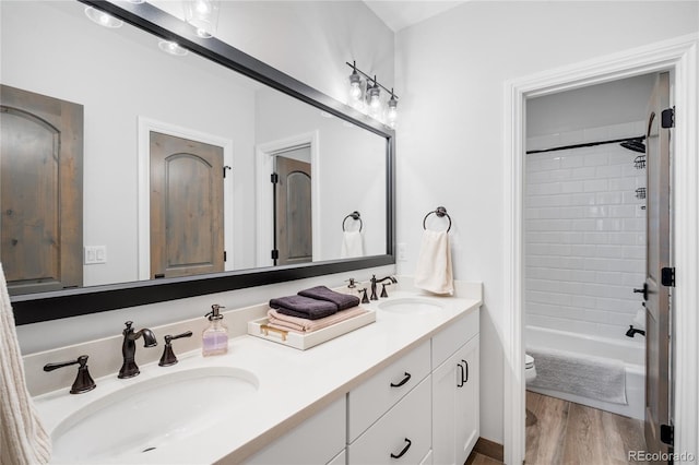 full bathroom featuring a sink, toilet, double vanity, and wood finished floors