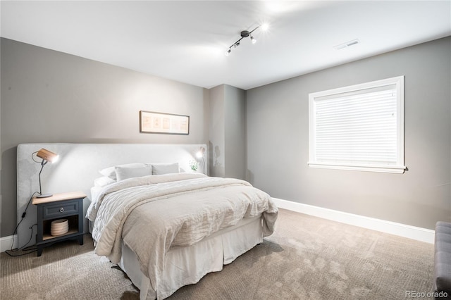 carpeted bedroom with baseboards, rail lighting, and visible vents
