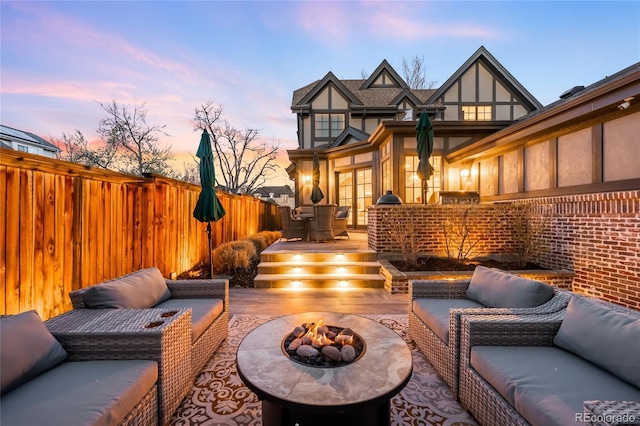 patio terrace at dusk featuring an outdoor living space with a fire pit, fence, and a deck