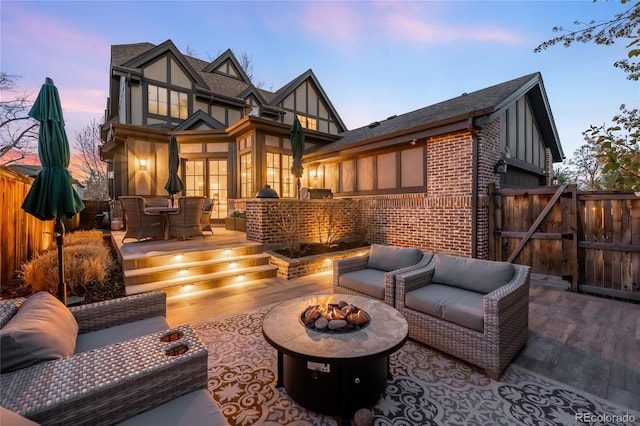 rear view of property with a gate, a patio area, brick siding, fence, and an outdoor living space with a fire pit