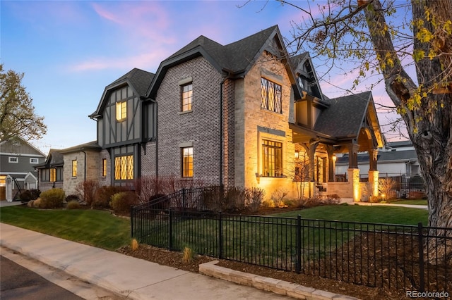 exterior space with a front yard, stone siding, brick siding, a shingled roof, and a fenced front yard